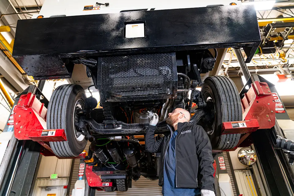 A man standing under a truck that is up on a lift.