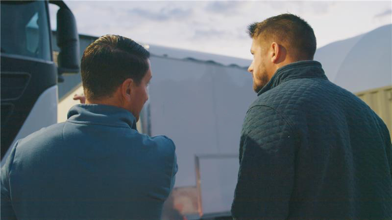 Two people facing away from the camera looking toward an electric truck