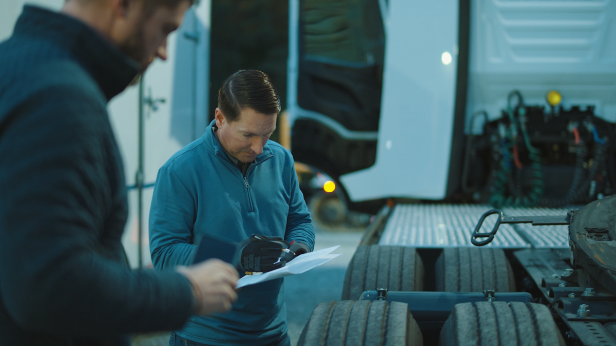 Two people standing next to the wheels of an electric truck looking at paperwork.