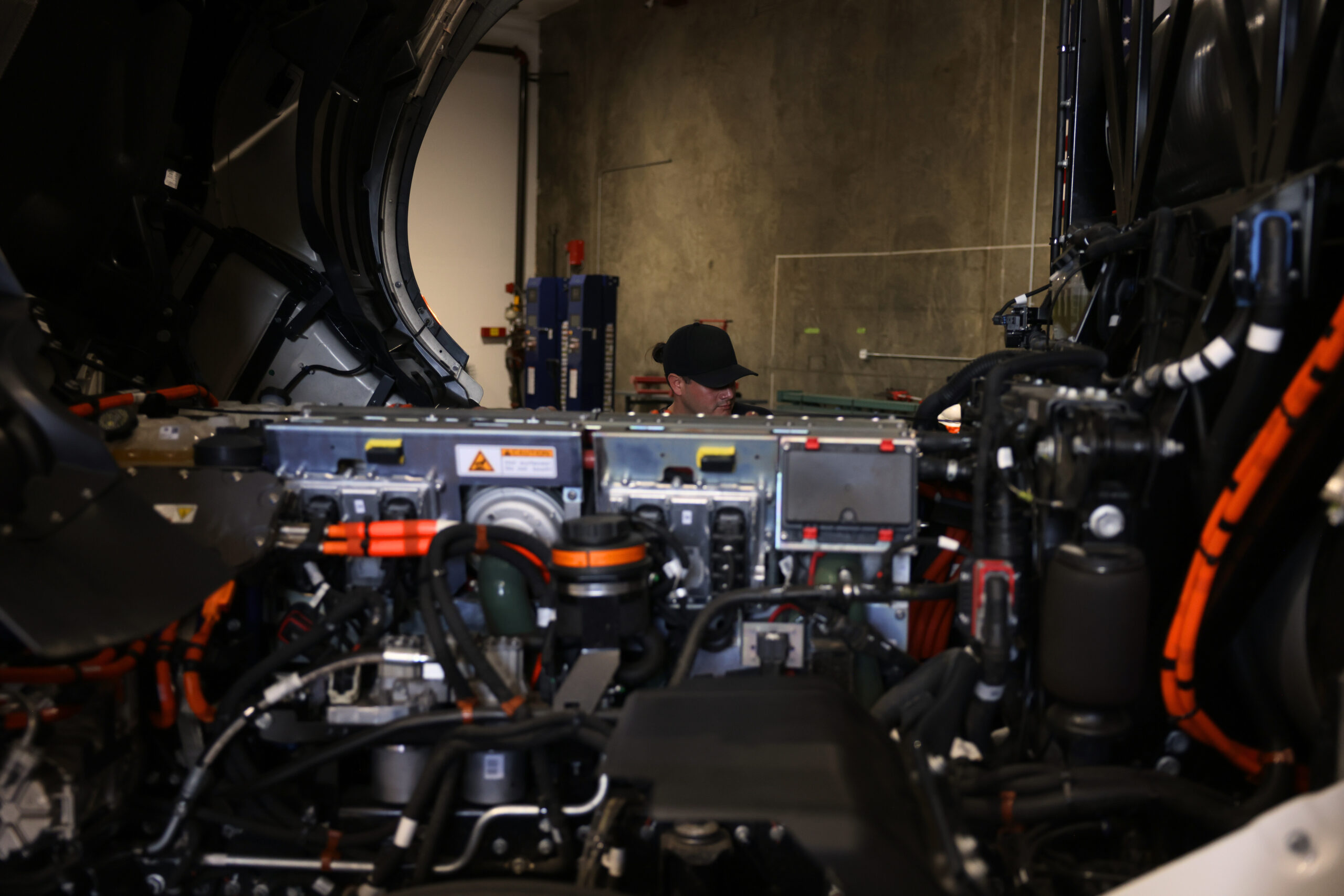 Image shows an open engine, with a repair technician in the background working on the engine.